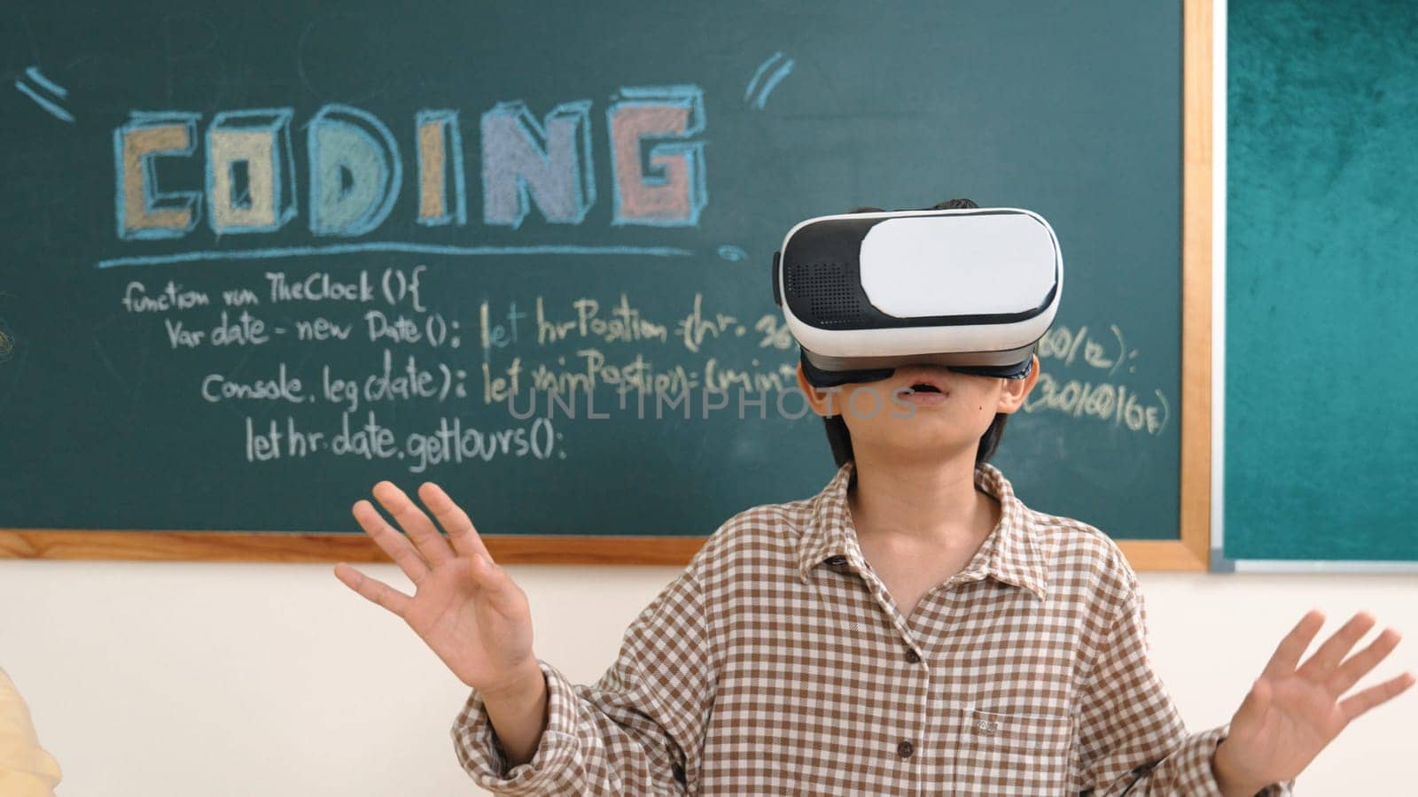 Energetic smart child wearing Vr headset while enter virtual world at classroom. Attractive asian elementary student using VR headset while learning about cyberspace and innovation program. Pedagogy.