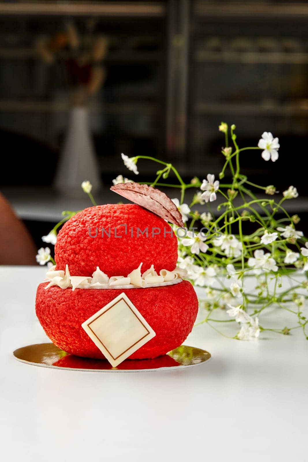 Tempting red choux pastry with crunchy craquelin with vanilla custard decorated with white chocolate petals and branded plaque on golden cardboard with delicate flowers. Signature handmade desserts