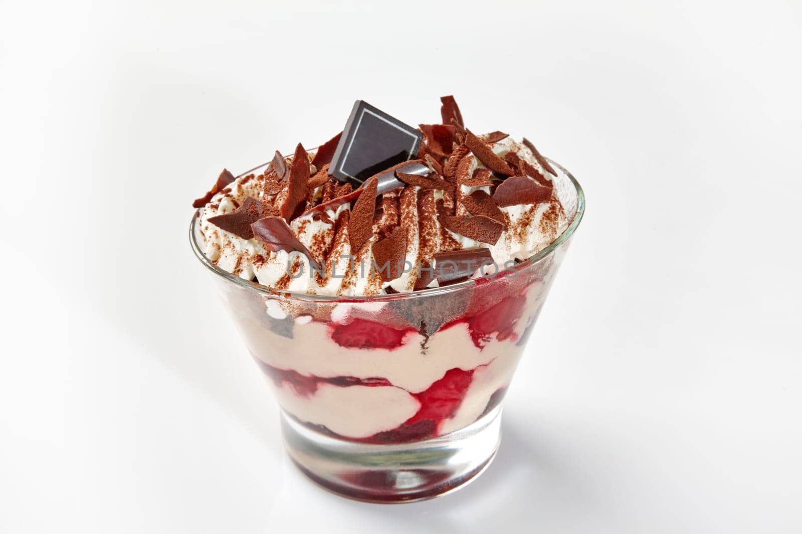 Luxurious chocolate and berry sundae with whipped cream, fresh cherries and chocolate shavings dusted with cocoa in clear dessert glass on white background