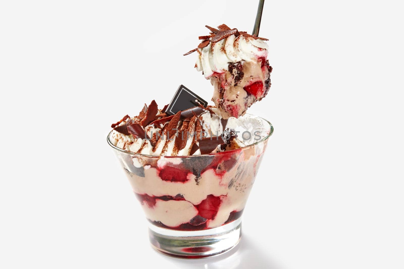 Appetizing layered dessert with chocolate sponge cake, ice cream and fresh cherries topped with whipped cream and chocolate shavings dusted with cocoa served in clear glass