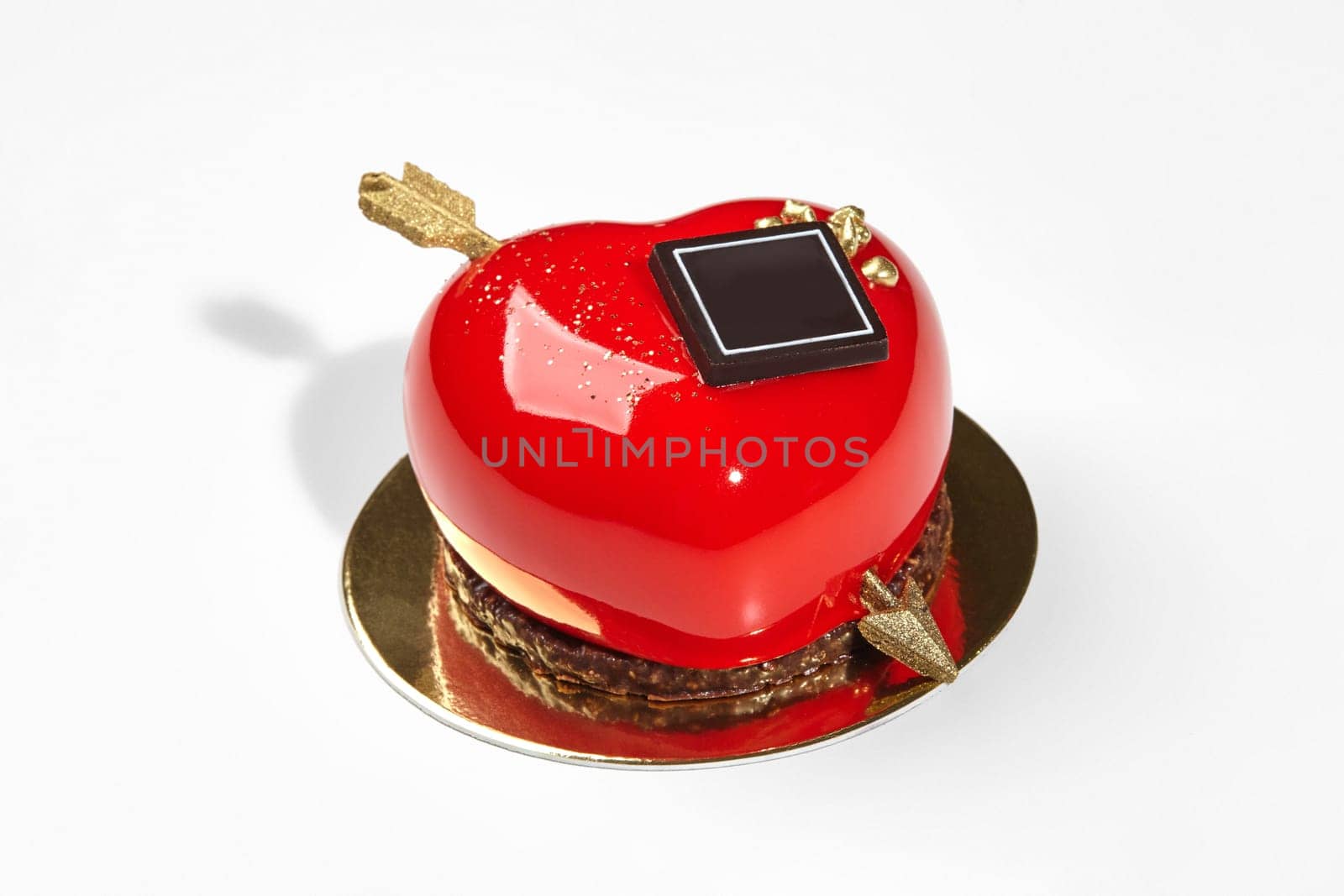 Vibrant red heart-shaped strawberry mousse cake with glossy icing, chocolate and golden arrow, perfect for celebrations of love and affection on Valentines Day, against white background