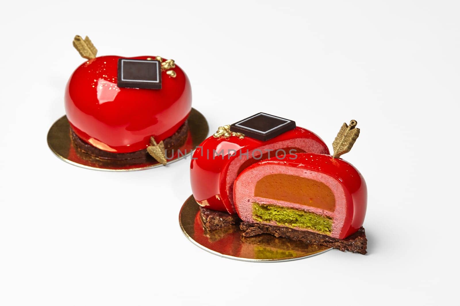 Delicate heart-shaped dessert of strawberry mousse with red glossy glaze, yogurt panna cotta and pistachio sponge layer decorated with gold arrow. Delicious romantic gift for Valentines Day