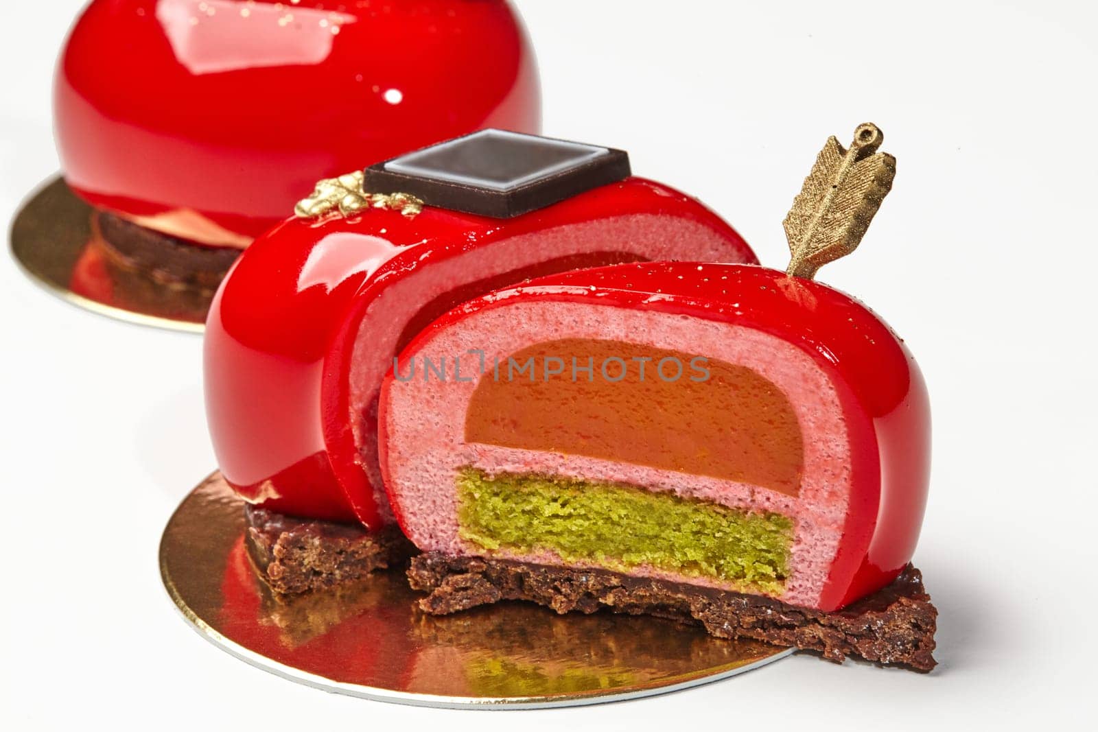 Delicious red glazed heart-shaped pastry with layers of strawberry mousse, sea buckthorn confit and pistachio sponge cake on chocolate streusel, decorated with golden arrow. Romantic dessert