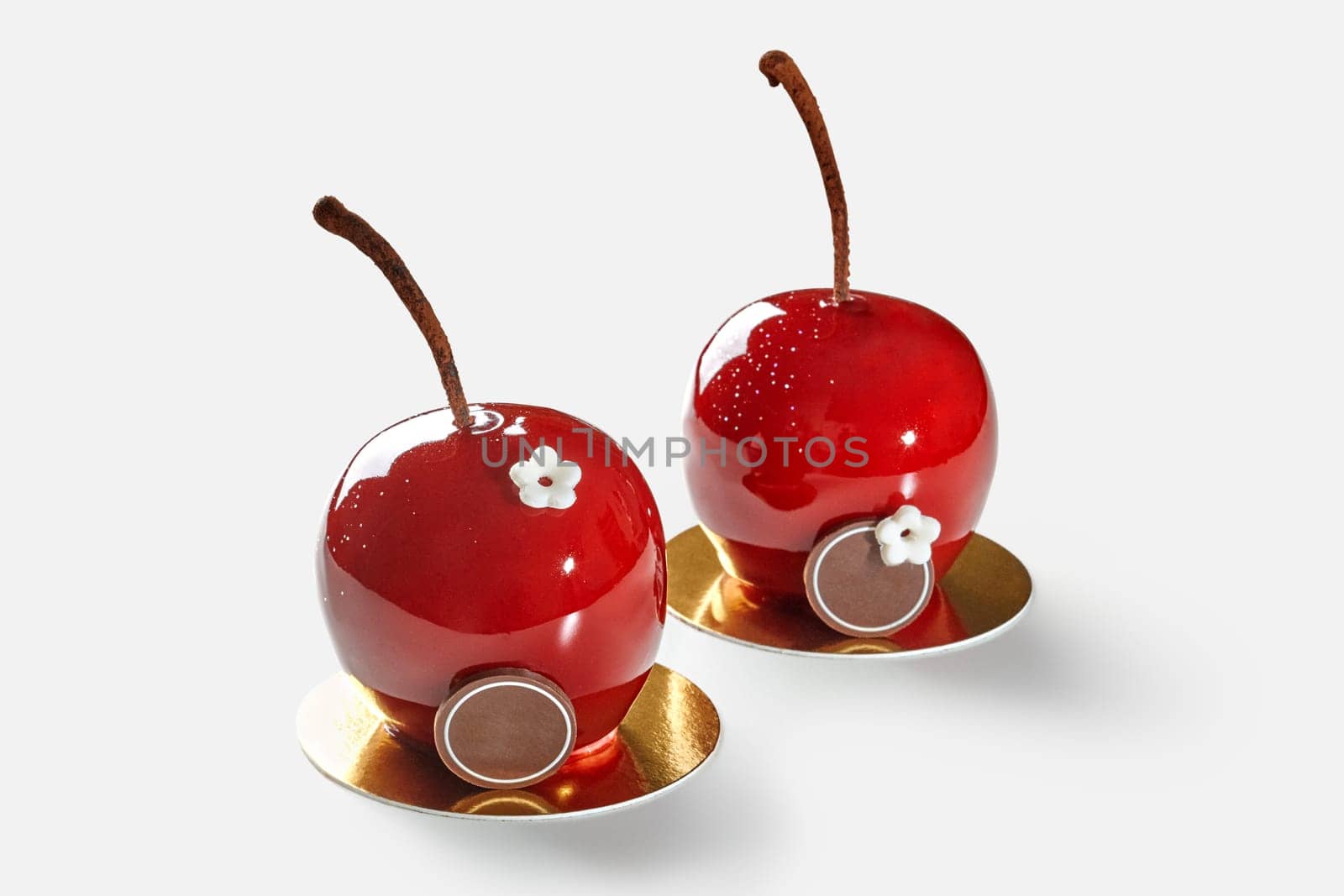 Tempting cherry-shaped pastries topped with red glossy glaze presented on gold cardboard cake base, isolated on white background. Artisan desserts concept