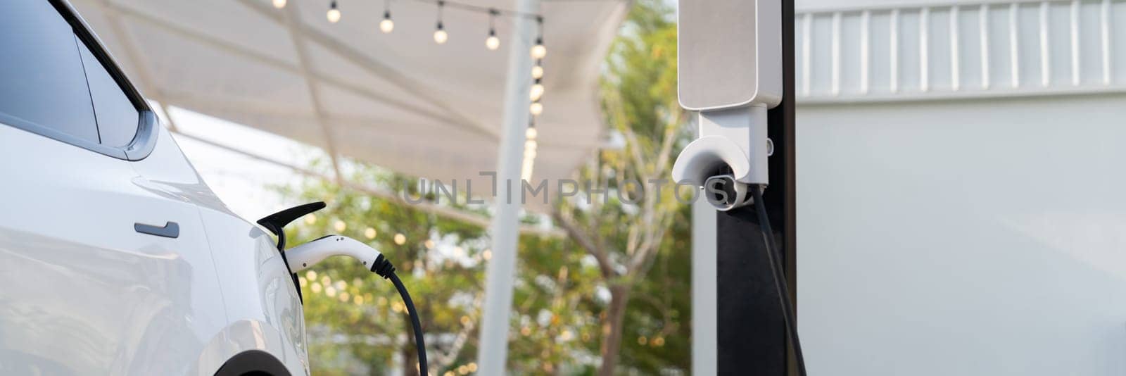 EV electric car recharge battery at parking lot in outdoor garden cafe. Alternative clean energy technology for rechargeable automobile for sustainable and eco friendly travel. Expedient