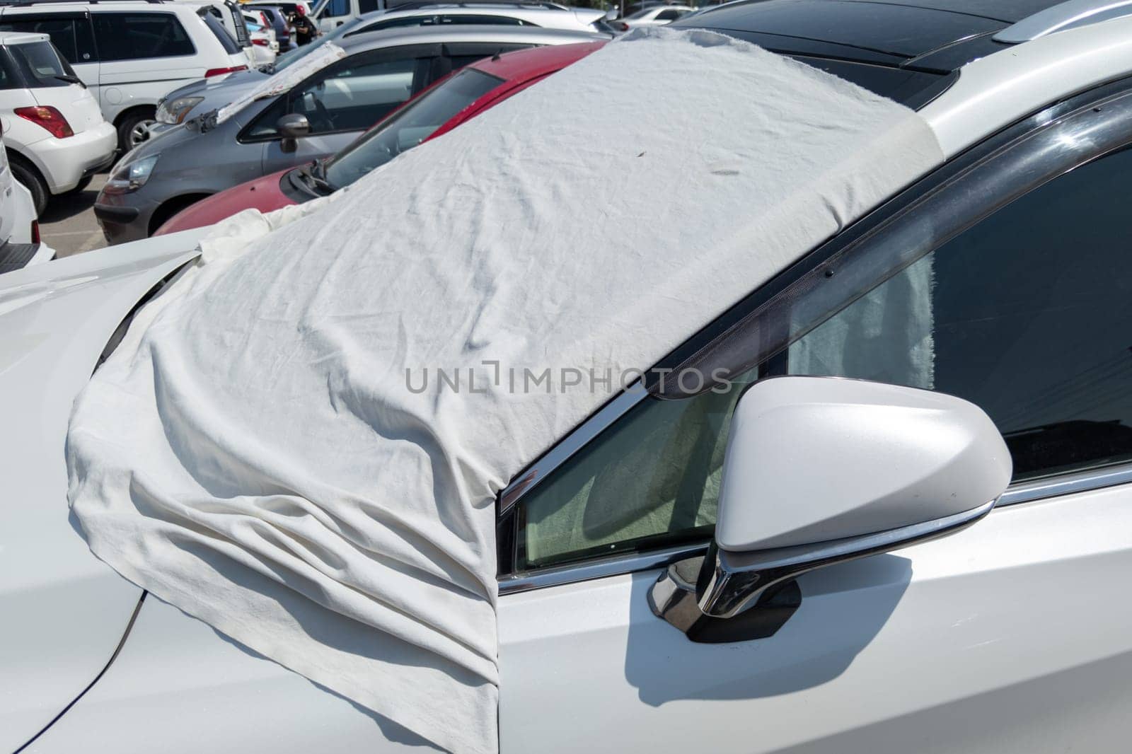 white car windshield is covered with white bedsheet to prevent heating on a parking lot at hot sunny summer day in Asia, closeup