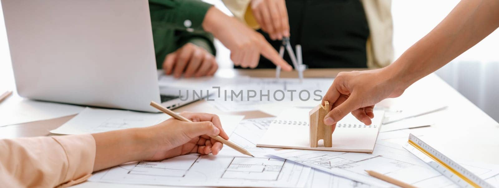 Professional architect team discussion about architectural project on meeting table with blueprint and wooden block scatter around at modern office. Closeup. Focus on hand. Delineation.