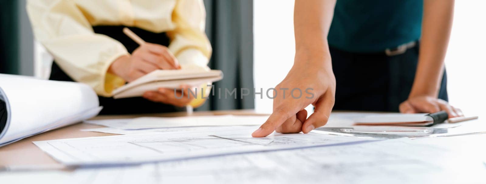 Skilled architect engineer team discuss about architectural project while project manager using laptop analysis data at meeting table with architectural document scatter around. Closeup. Delineation.