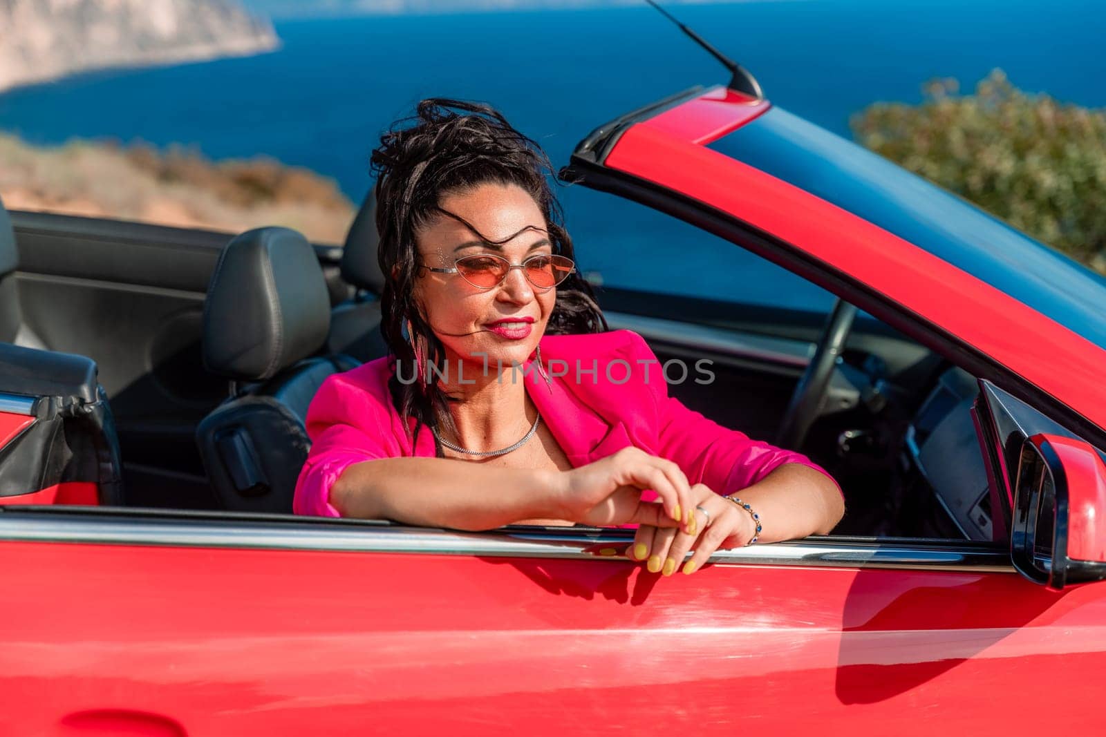 A woman in a pink jacket is sitting in a red convertible. She is wearing sunglasses and has her hand on her hip. Scene is relaxed and carefree. by Matiunina