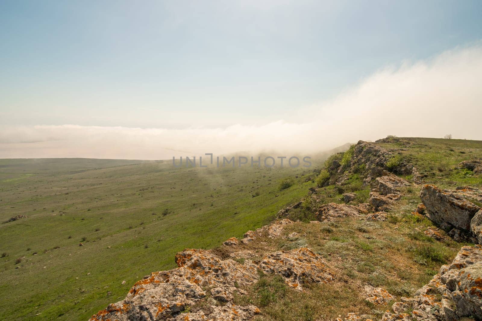 A foggy mountain top with a clear blue sky in the background. The sky is filled with clouds, giving the scene a serene and peaceful atmosphere