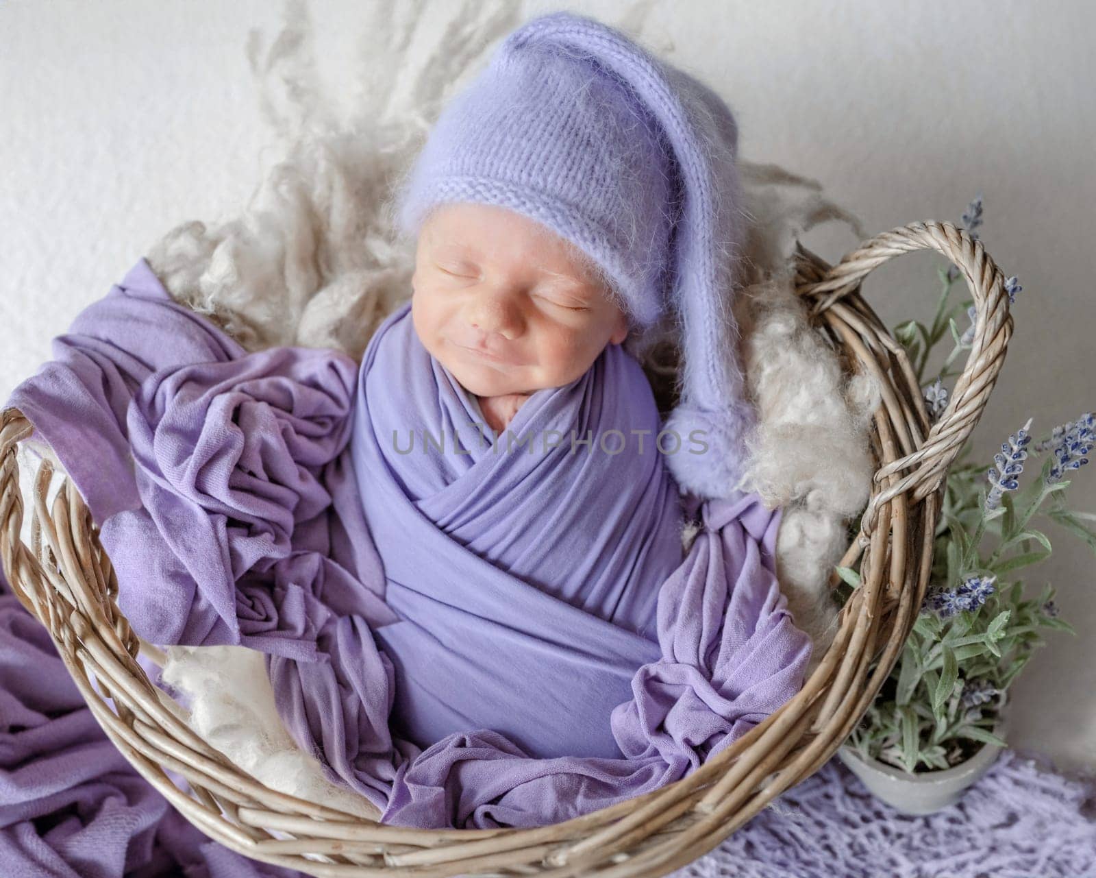 Newborn Baby Wrapped In Lavender Sleeps In A Basket During A Studio Photoshoot