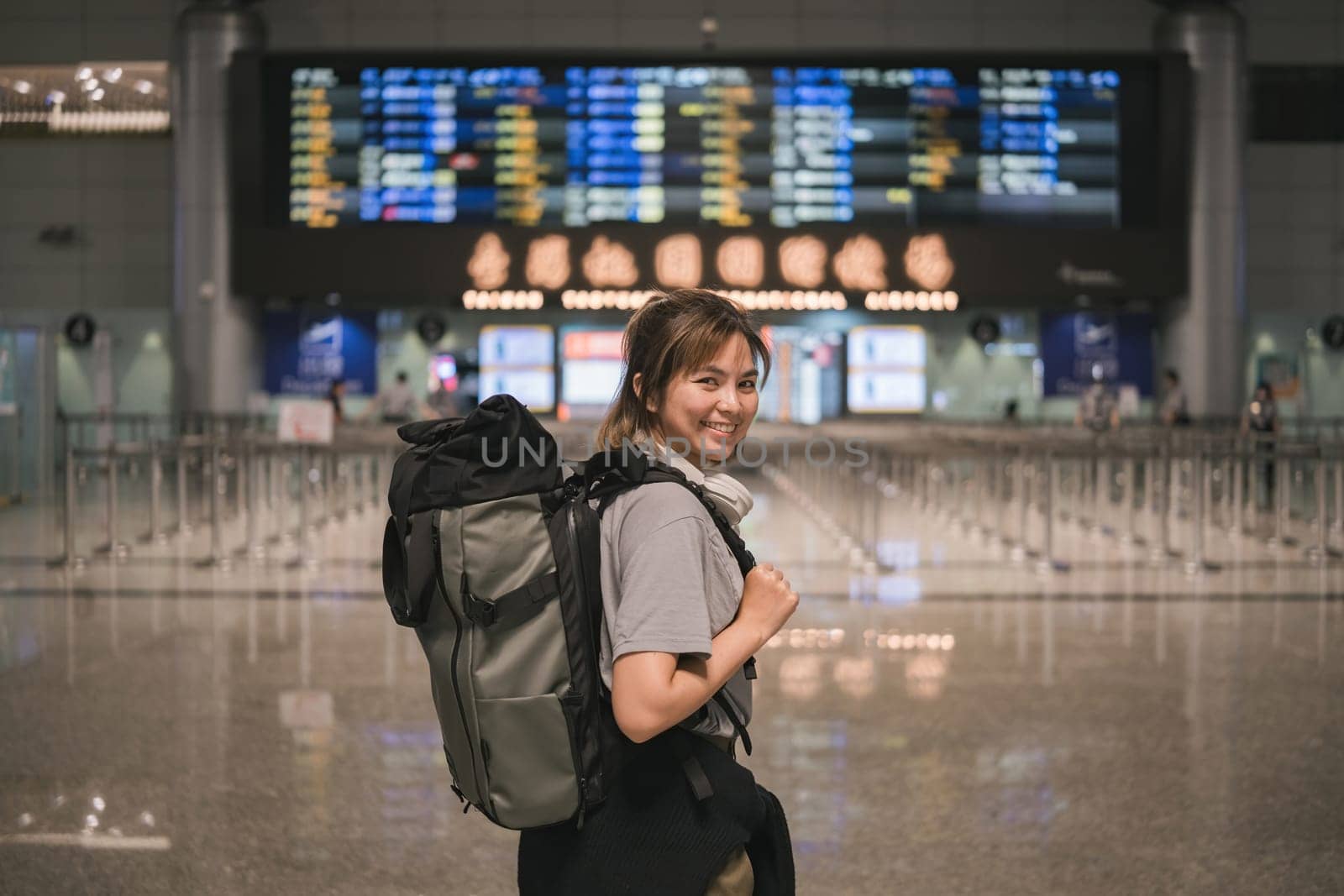 Young Asian woman in international airport looking at flight information board, checking her flight.