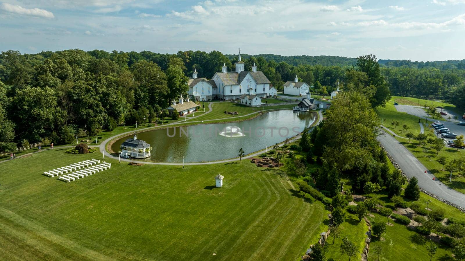 Elizabethtown, Pennsylvania, USA, August 11, 2023 - Aerial View Showcasing A Cluster Of Traditional White Orthodox Churches With Cross-Topped Domes, Arranged Around A Curved Pond With A Fountain, Amidst Green Trees And Neatly Arranged White Benches