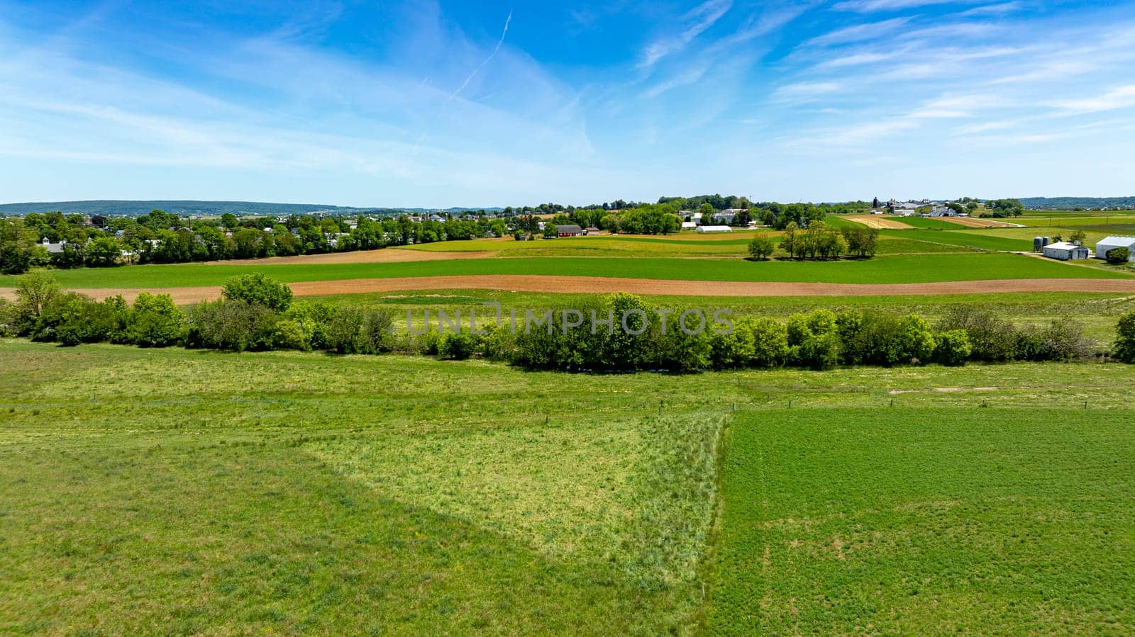 A large field with a few houses in the distance. The sky is blue and the grass is green