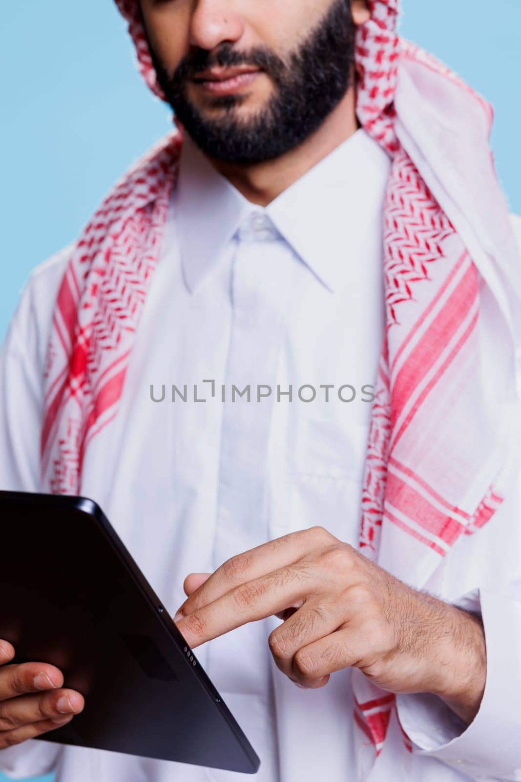 Man dressed in islamic clothes using digital tablet and making touch gesture closeup. Arab person wearing traditional white thobe and ghutra headdress scrolling page with two fingers