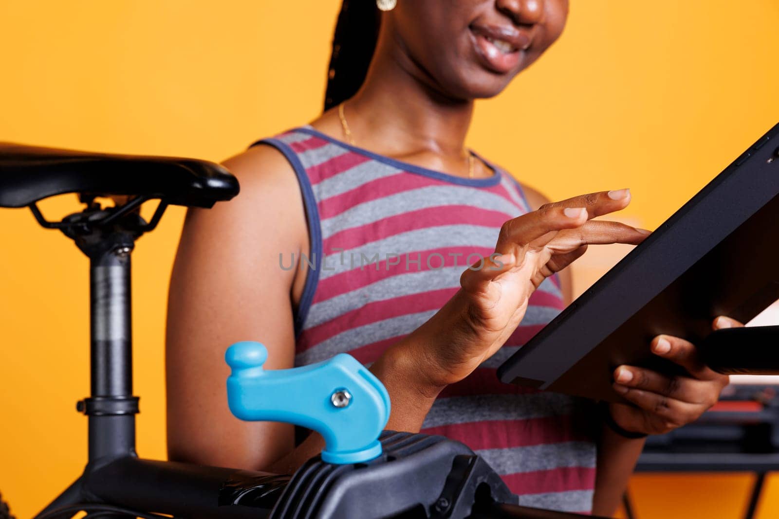 Detailed view of youthful black woman looking for bike maintenance on her phone tablet. Close-up of an African-American female cyclist carrying a smart device while examining her bicycle.