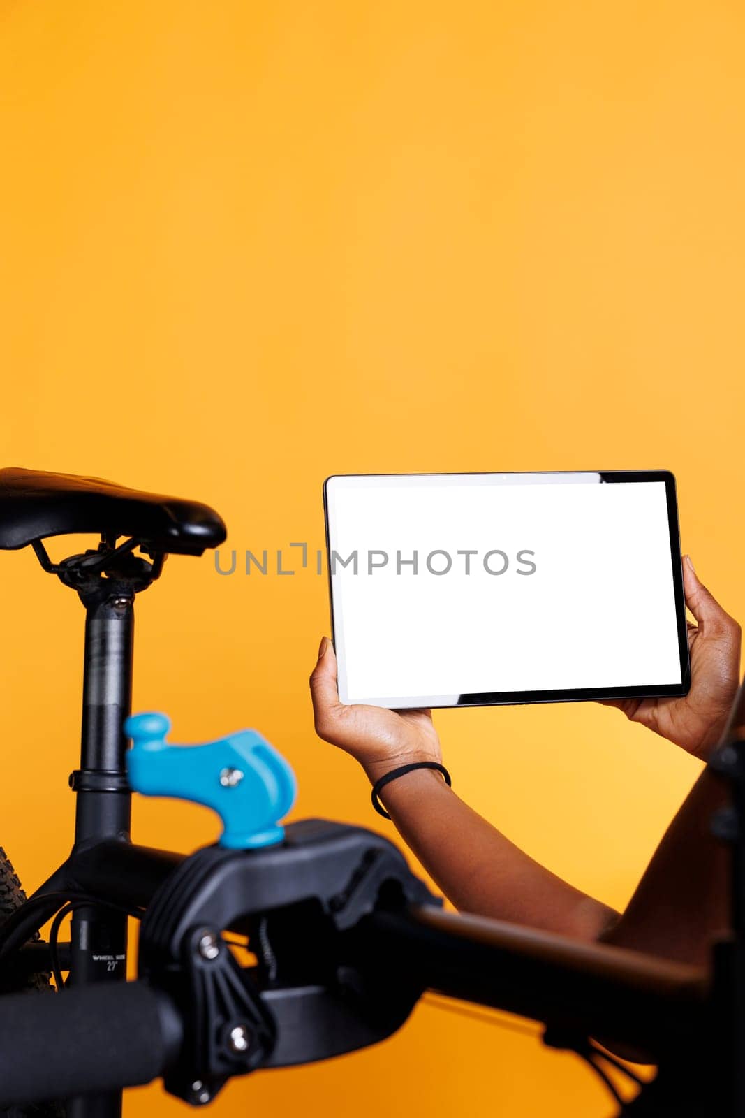 Close-up shot of tablet with isolated chromakey template carried by african american female cyclist. In front of yellow background, a black person is holding a device displaying blank whitescreen.