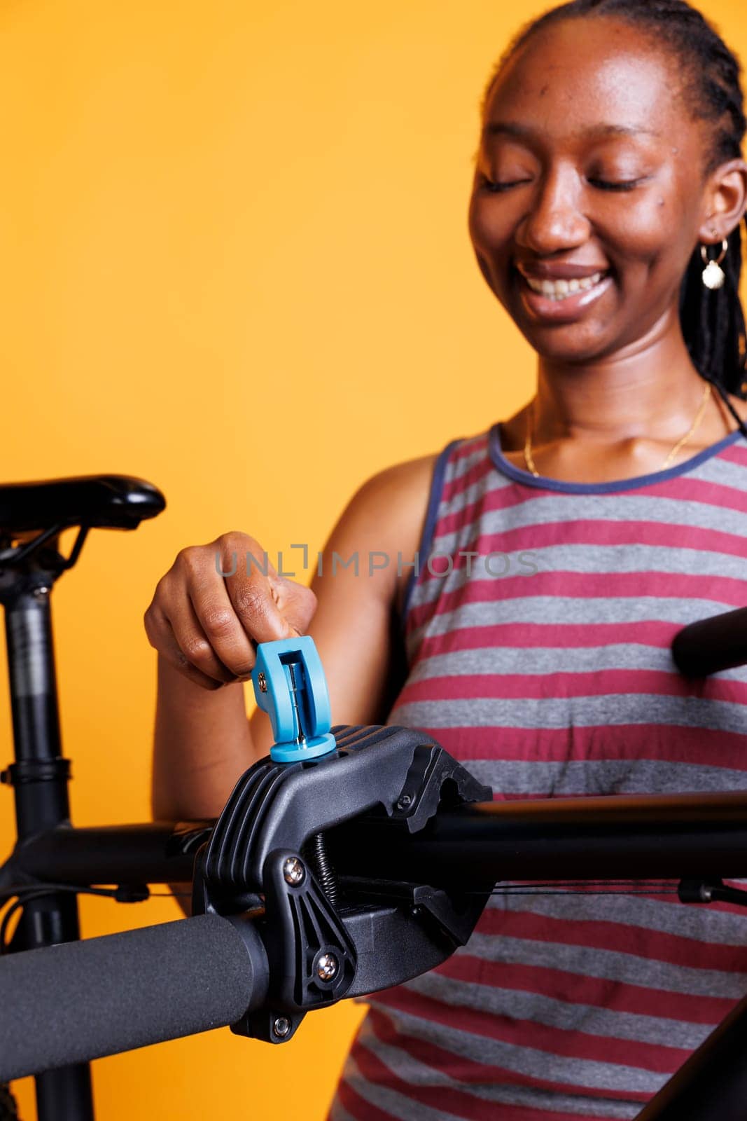Detailed view of african american female examining, adjusting, and fixing bicycle to ensure safety. Image showing black woman gripping and fastening a broken bike onto a repair stand. Close-up shot.