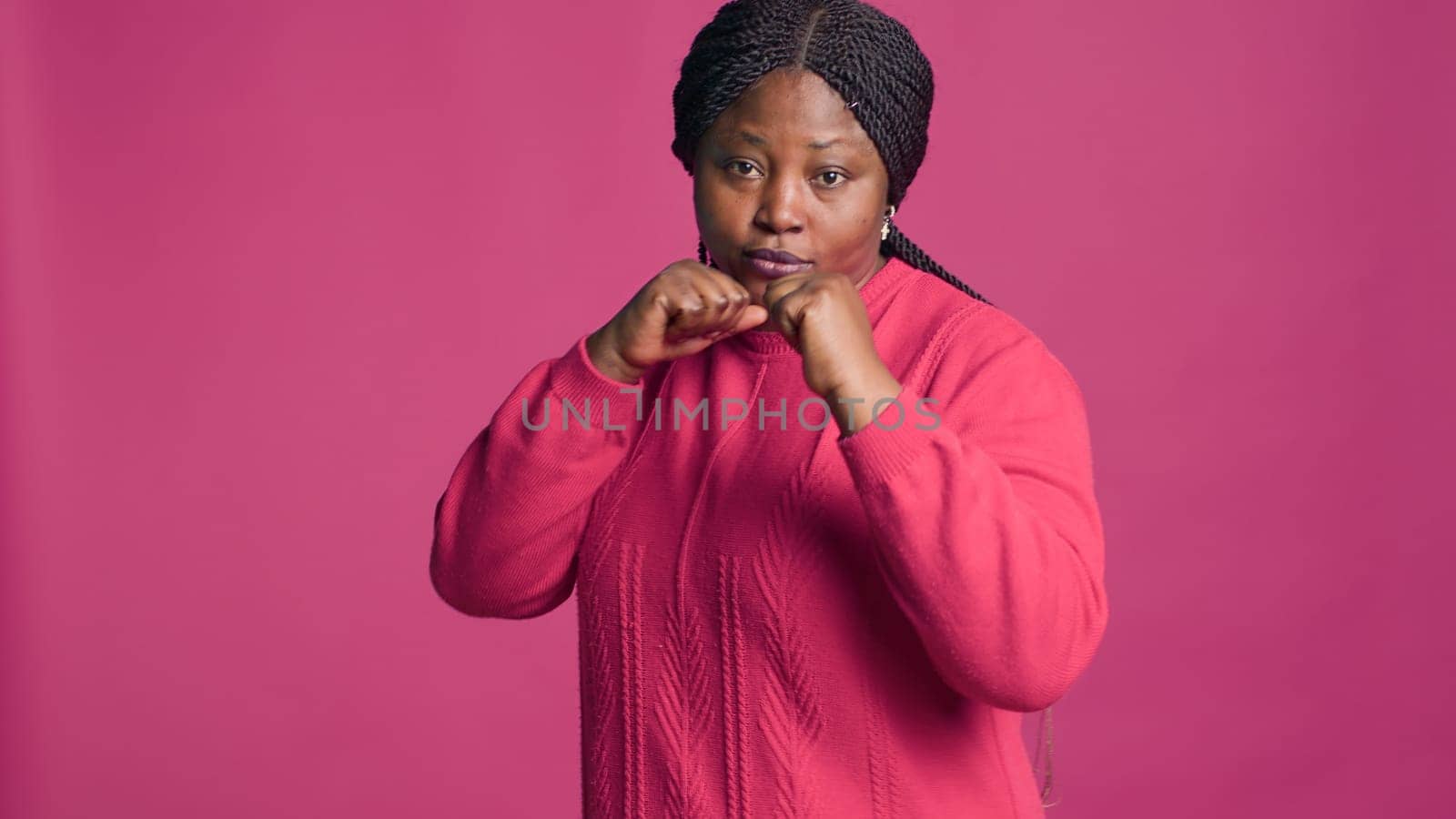 Confident black woman with her hands clasped together showing ready for fighting. African american lady with self-confidence posing with clenched fists against pink color background.