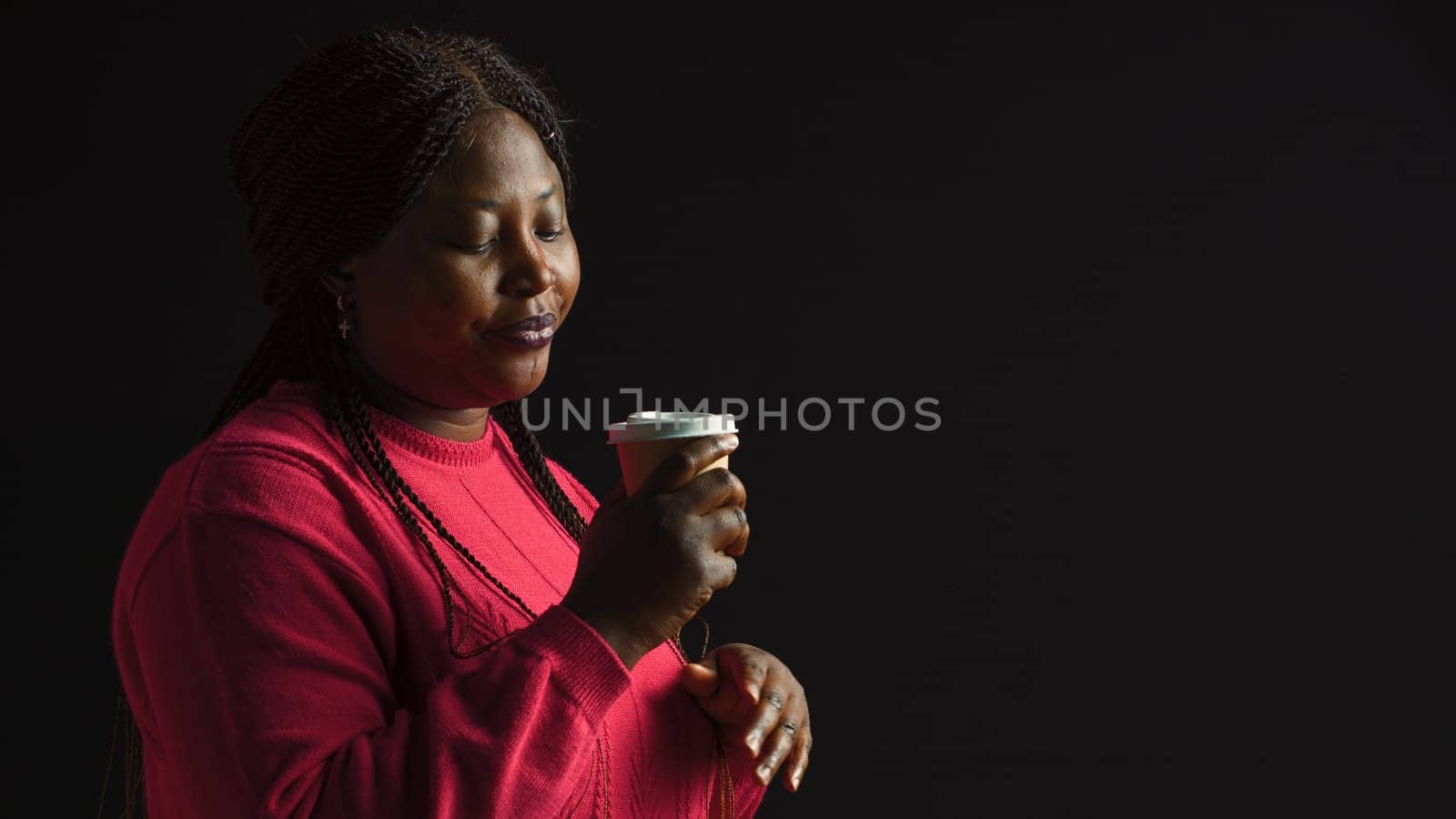 African american woman immersed in pleasure of sipping coffee lost in contemplation gazing upwards. Female fashion blogger savors her warm beverage with sense of satisfaction. Side-view portrait.