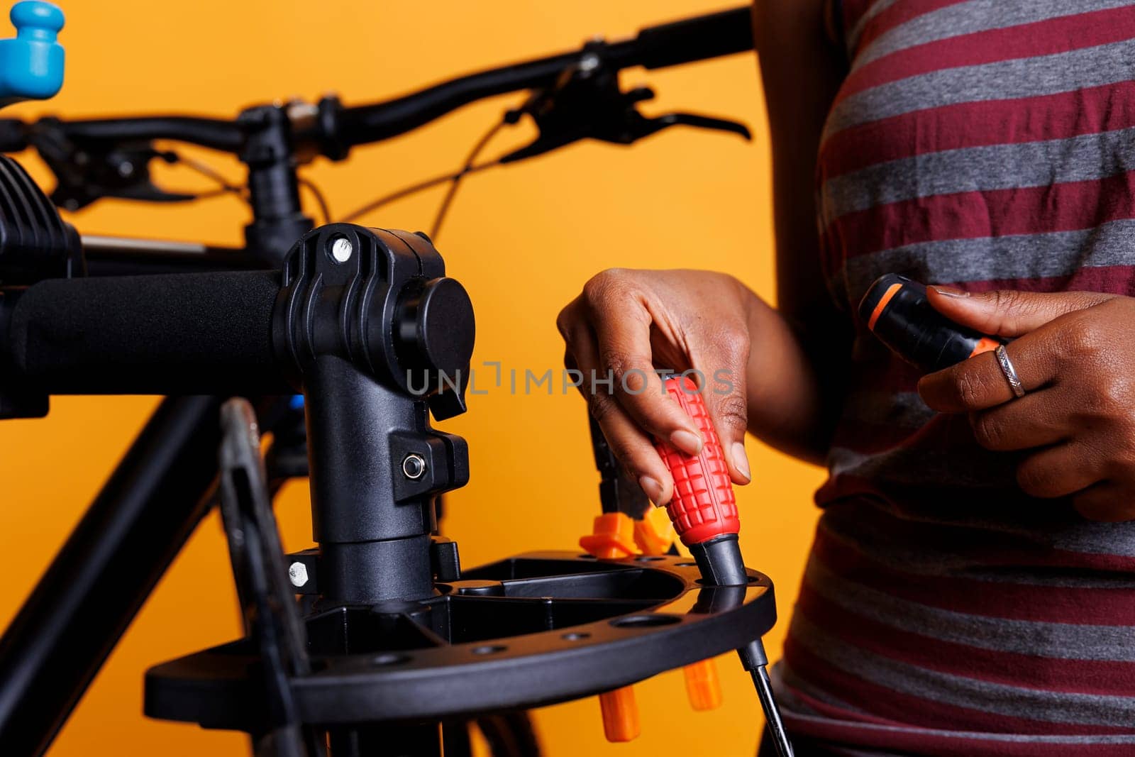 Close-up of african american female hand organizing necessary bicycle service tools. Photo focus on screwdriver and other specialized equipments being arranged on bike repair-stand by an individual.