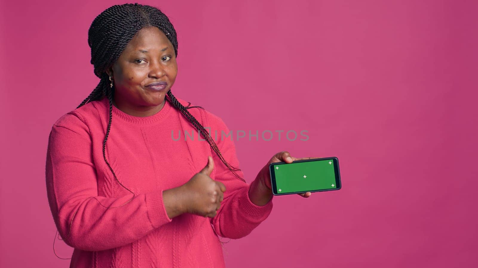 Enthusiastic black woman horizontally grasping cell phone with blank chromakey template. Positive african american lady carrying mobile phone showing isolated green screen display.