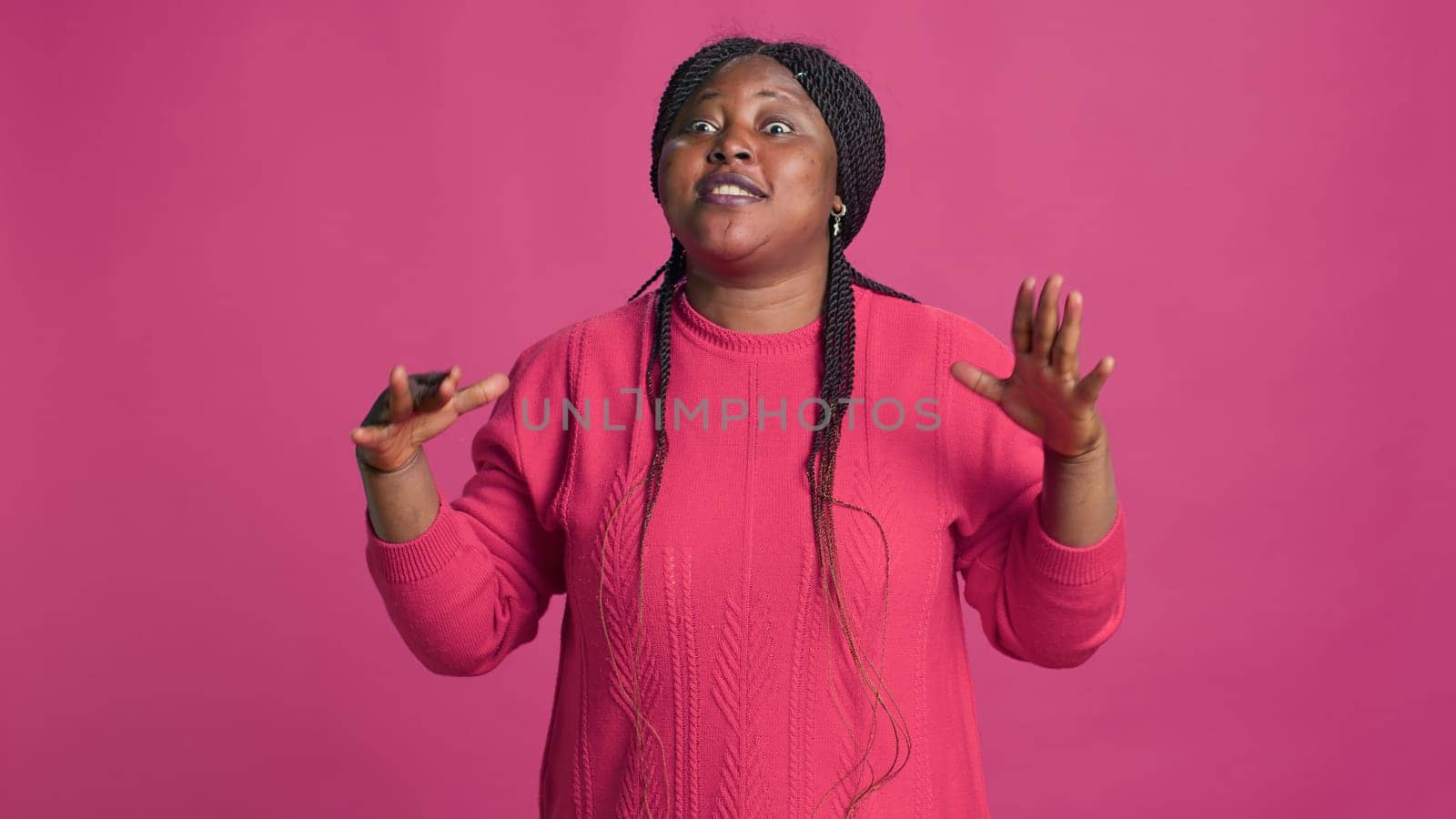 African american female in pink sweater with hands covering her face expressing anger and annoyance. Young woman fashion influencer screaming no while looking at camera.