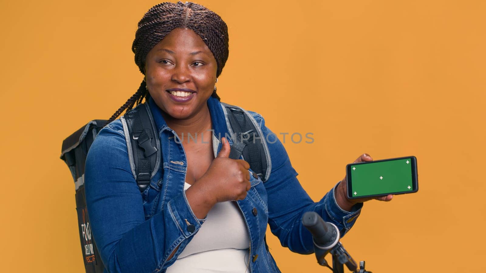 Friendly black woman horizontally carrying delivery cell phone device displaying isolated mockup template. African american courier gripping digital phone with green screen display. Handheld shot.