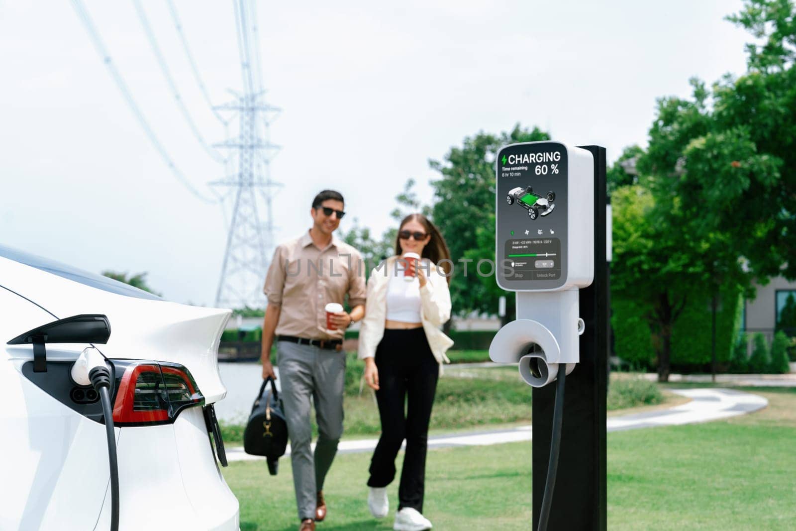 Young couple with coffee recharge EV car battery at charging station connected to electrical industrial power grid tower. Couple with shopping and travel using eco electric car lifestyle. Expedient