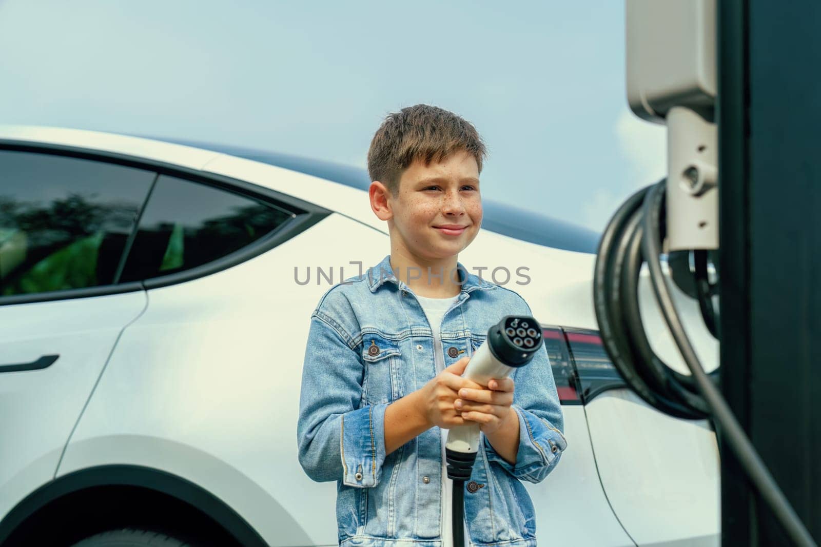 Little boy recharging eco-friendly electric car from EV charging station. EV car road trip travel concept for alternative transportation powered by clean renewable and sustainable energy. Perpetual