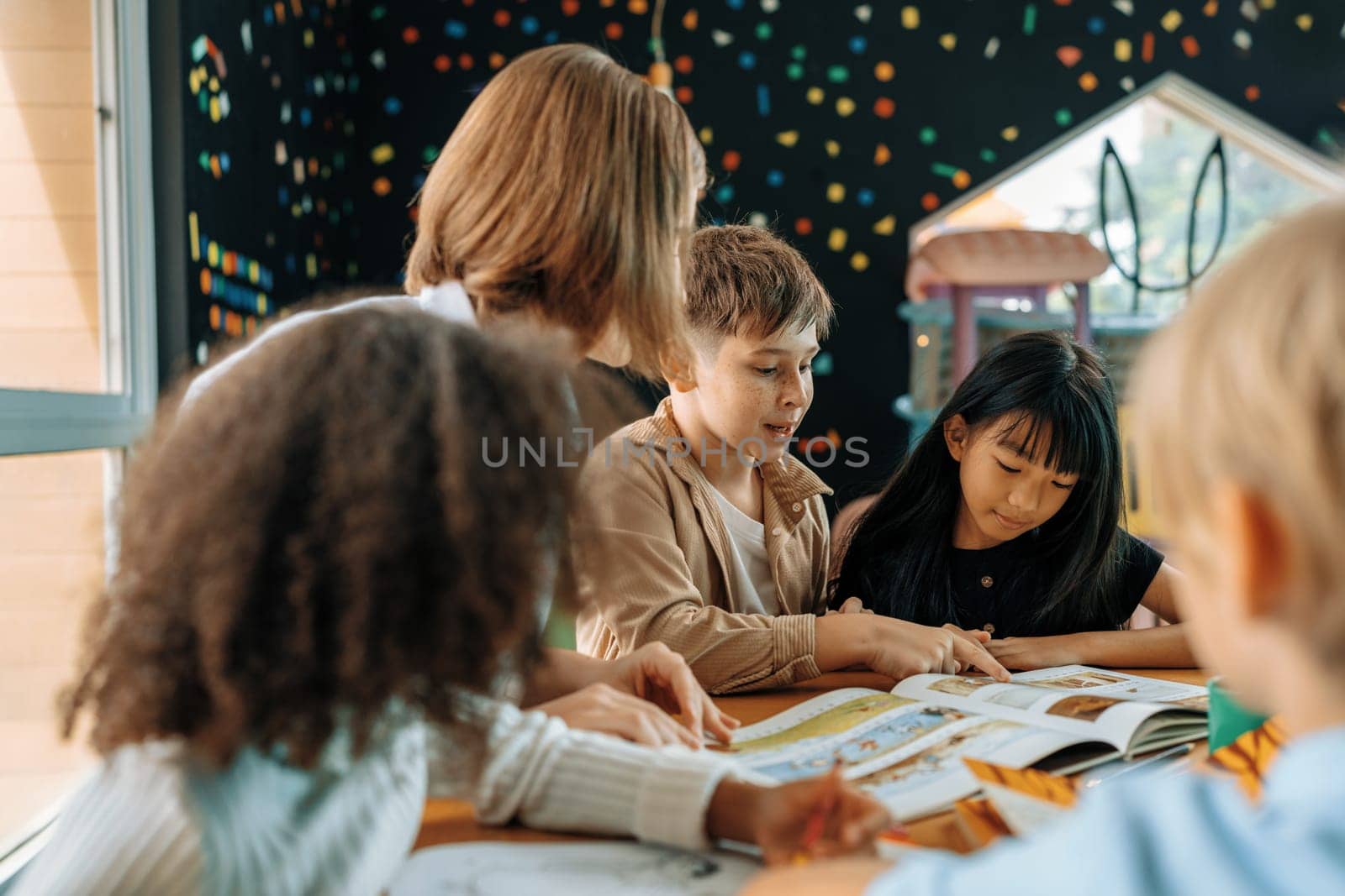 Teacher is teaching student about lesson from the books in the classroom, the children are happy. Some ask teacher, a boy in blue shirt is reading a book on his own and a girl is drawing. Erudition.