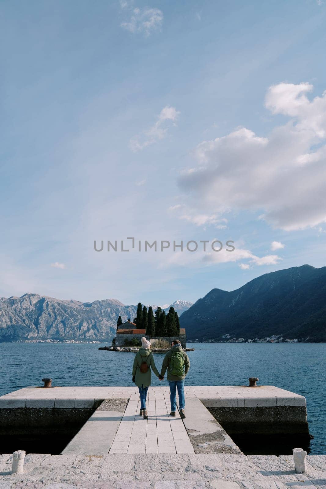 Man and woman walk holding hands along the pier looking out over St. George Island. Back view. Montenegro. High quality photo