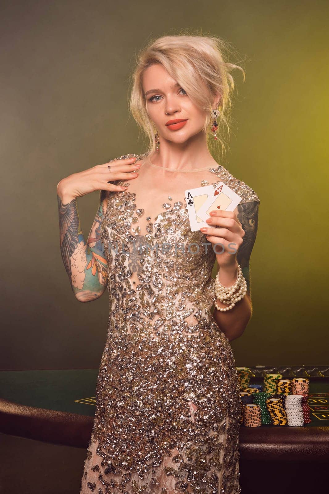 Blonde woman with a beautiful hairstyle and perfect make-up is posing with two playing cards in her hands. Casino, poker. by nazarovsergey
