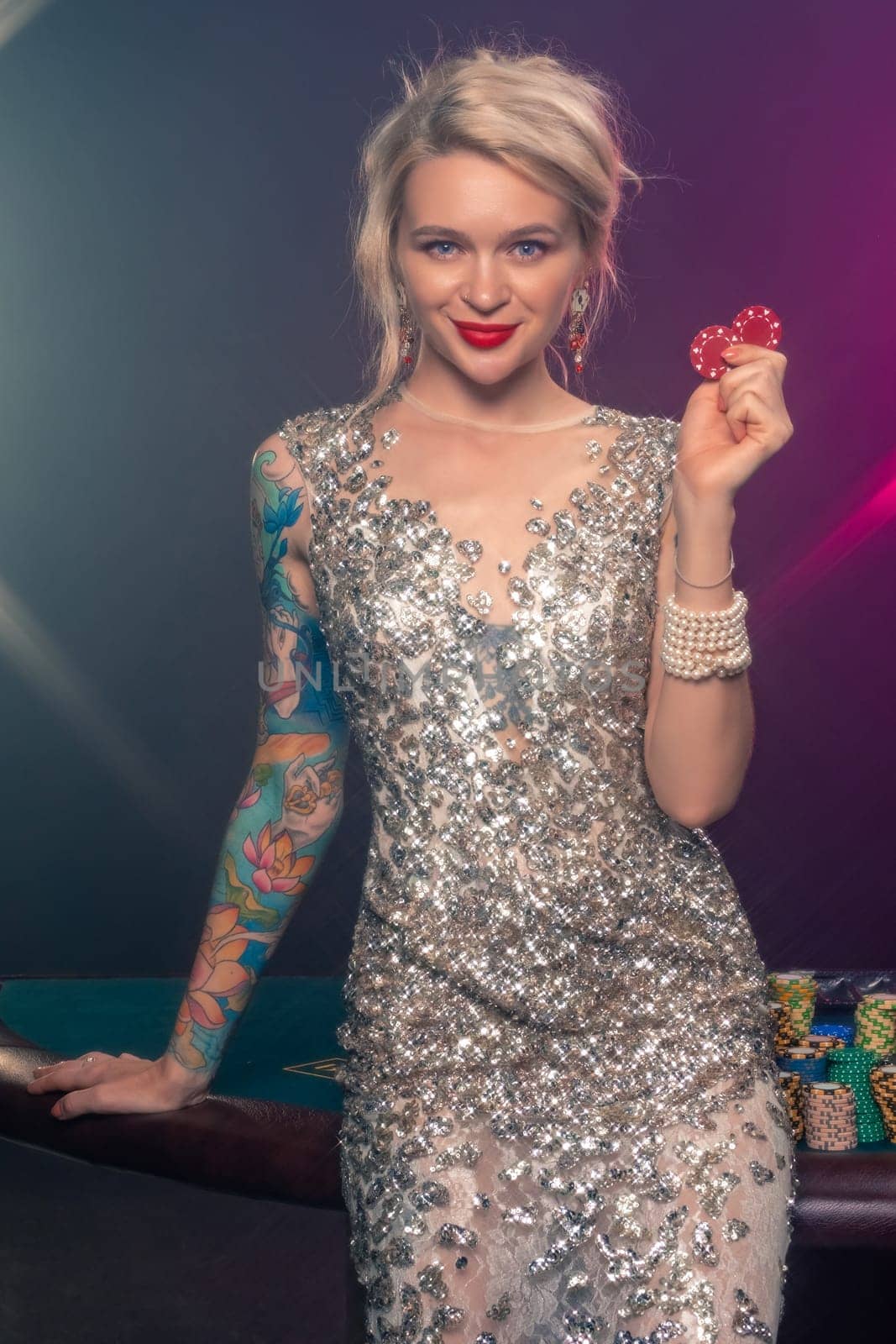 Blonde woman with a beautiful hairstyle and perfect make-up is posing with red gambling chips in her hands. Casino, poker. by nazarovsergey