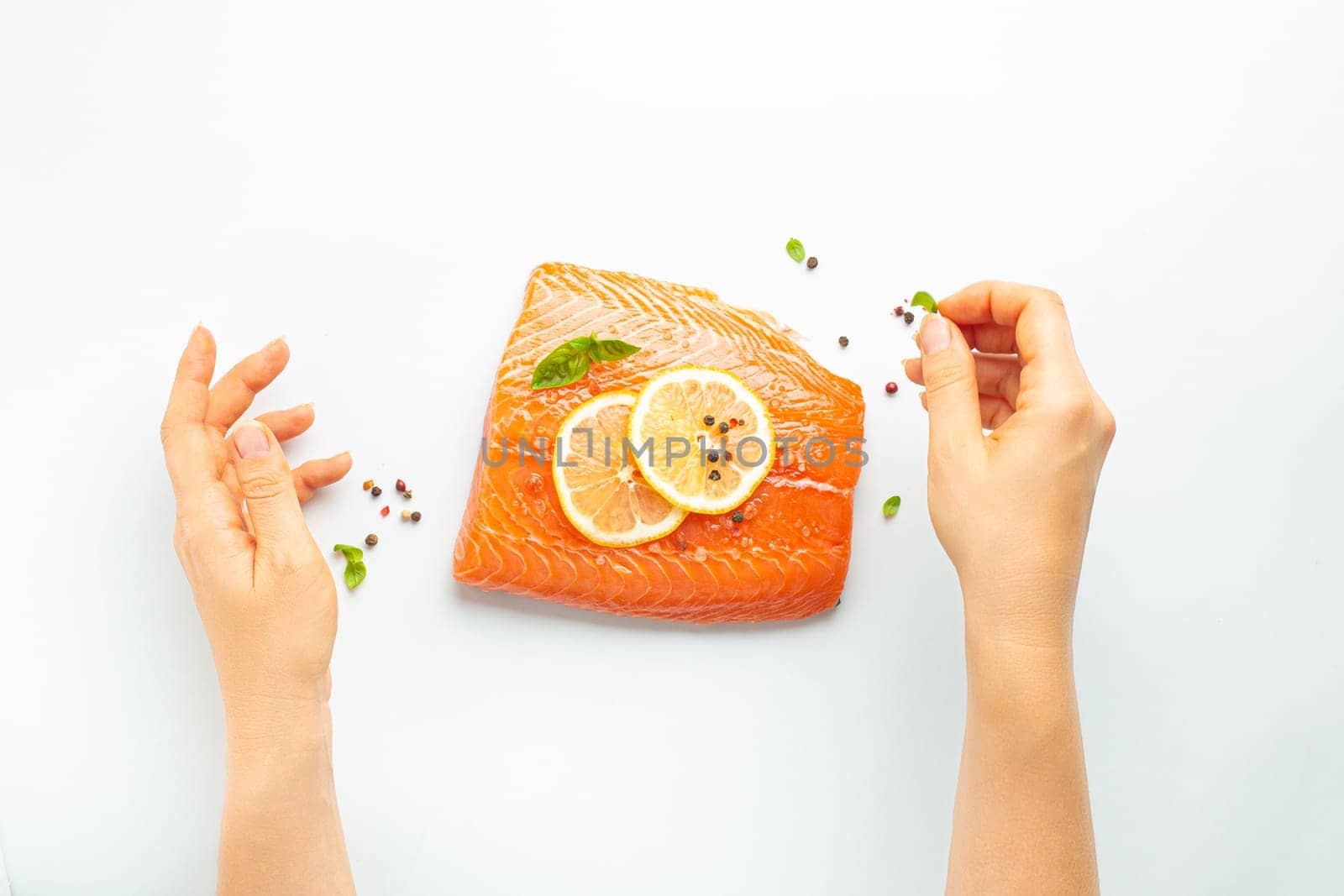 Female hands seasoning fresh raw salmon marbled fillet isolated on white background with lemon, coarse salt, green herbs top view. Healthy nutrition and balanced diet by its_al_dente