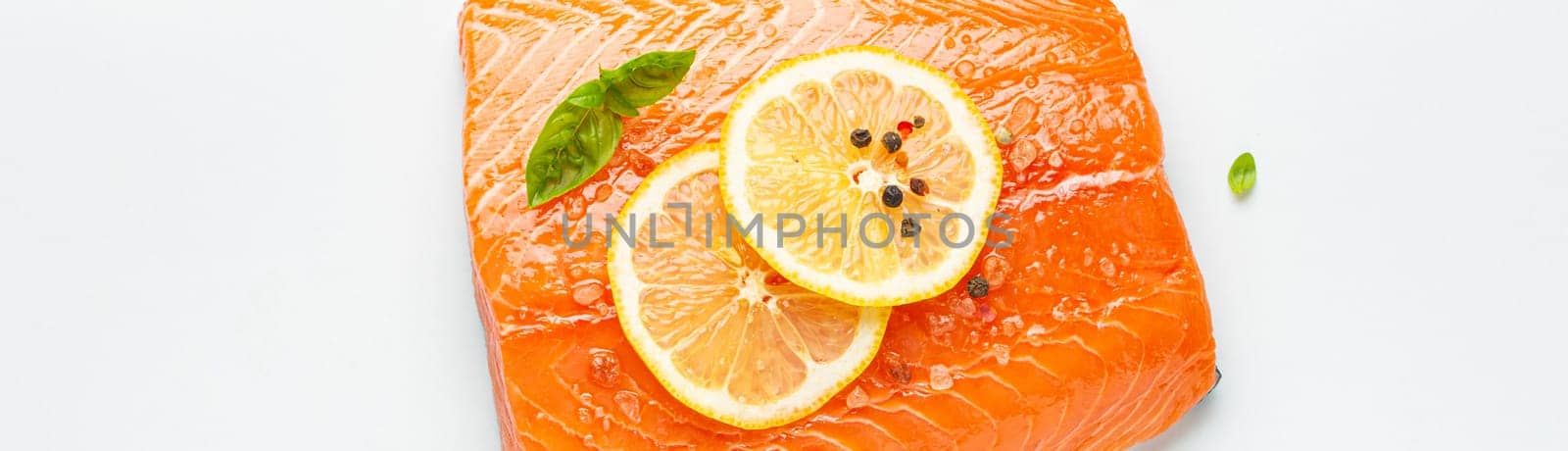 Fresh raw salmon marbled fillet isolated on white background with lemon, coarse salt, green herbs top view. Healthy nutrition and balanced diet.
