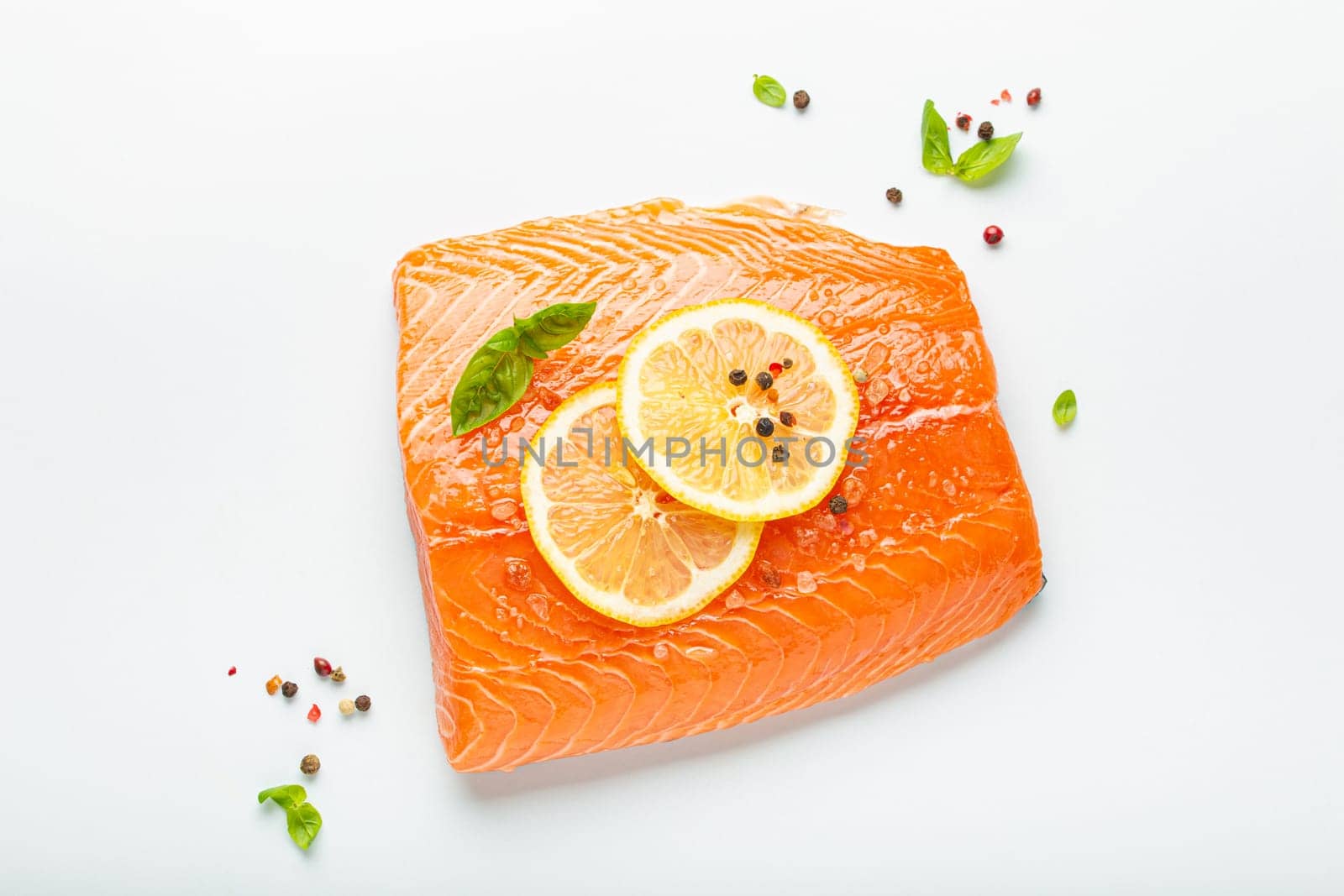 Fresh raw salmon marbled fillet isolated on white background with lemon, coarse salt, green herbs top view. Healthy nutrition and balanced diet.