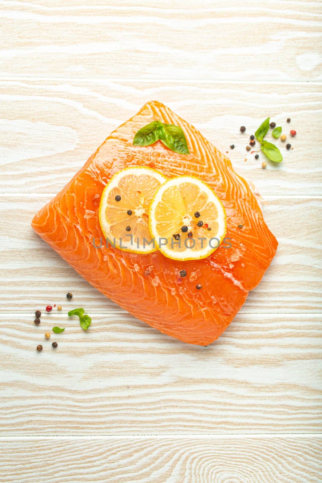 Fresh raw salmon marbled fillet on white rustic wooden table background with lemon, coarse salt, green herbs top view. Healthy cooking and balanced diet.