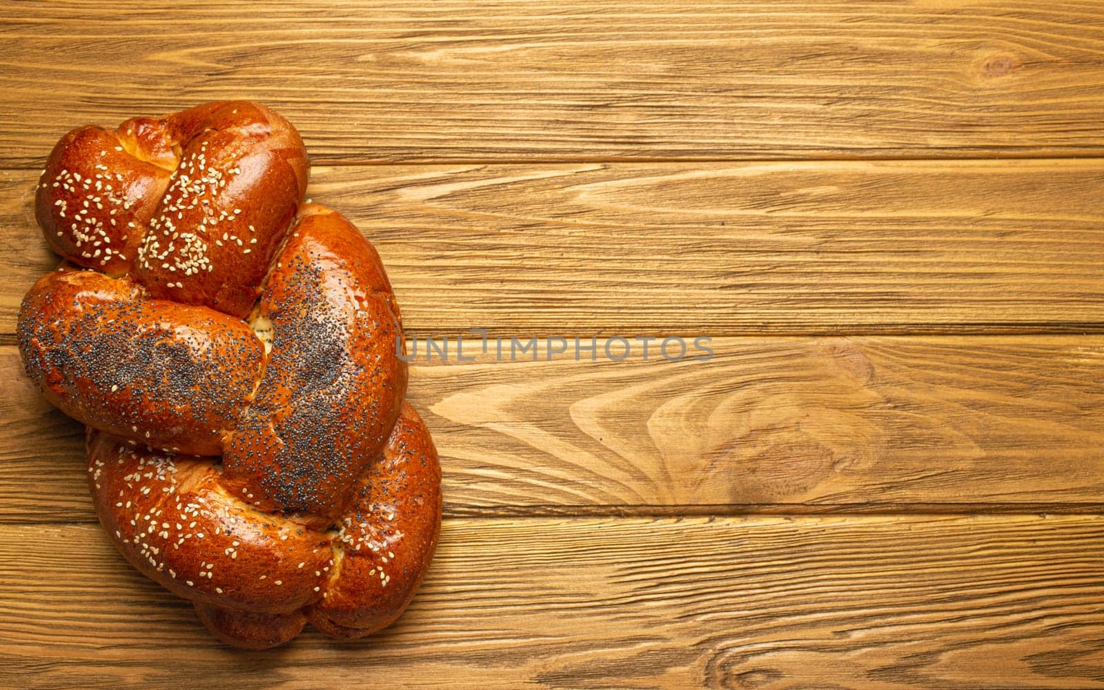 Freshly baked Challah bread covered with poppy and sesame seeds, top view on rustic wooden background, traditional festive Jewish cuisine. Space for text by its_al_dente