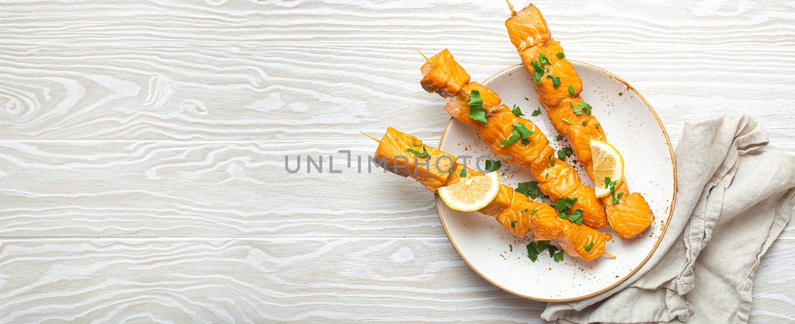Grilled barbecue salmon skewers seasoned with green parsley and lemon on ceramic plate on white wooden rustic table background top view, healthy eating by its_al_dente