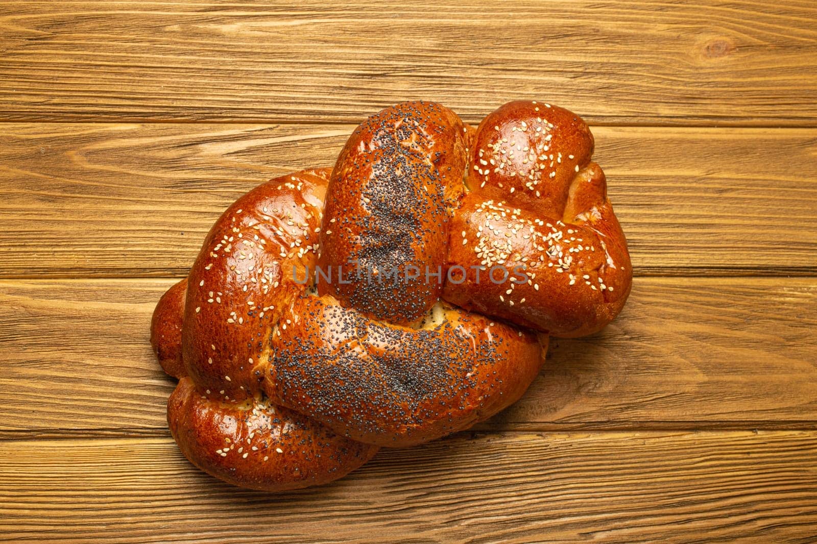 Freshly baked Challah bread covered with poppy and sesame seeds, top view on rustic wooden background, traditional festive Jewish cuisine.