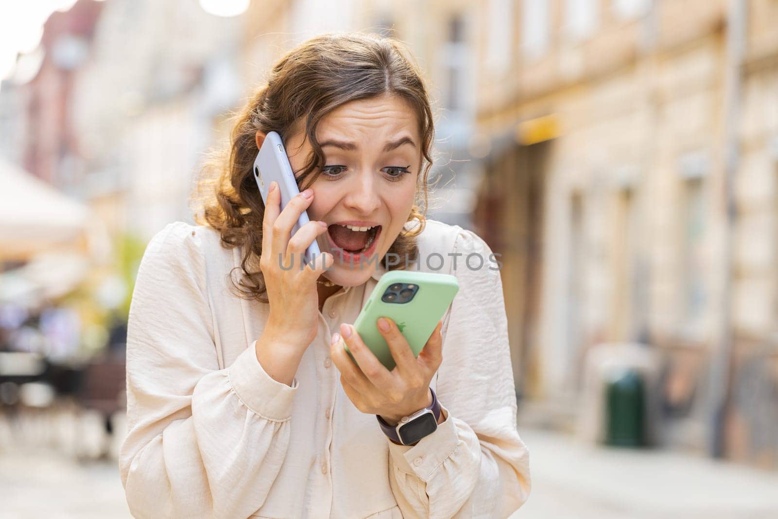 Irritated nervous stressed young woman talking screaming on two mobile phones having conversation conflict quarrel complaint dispute discuss solve problem outdoors. Girl walking in urban city street