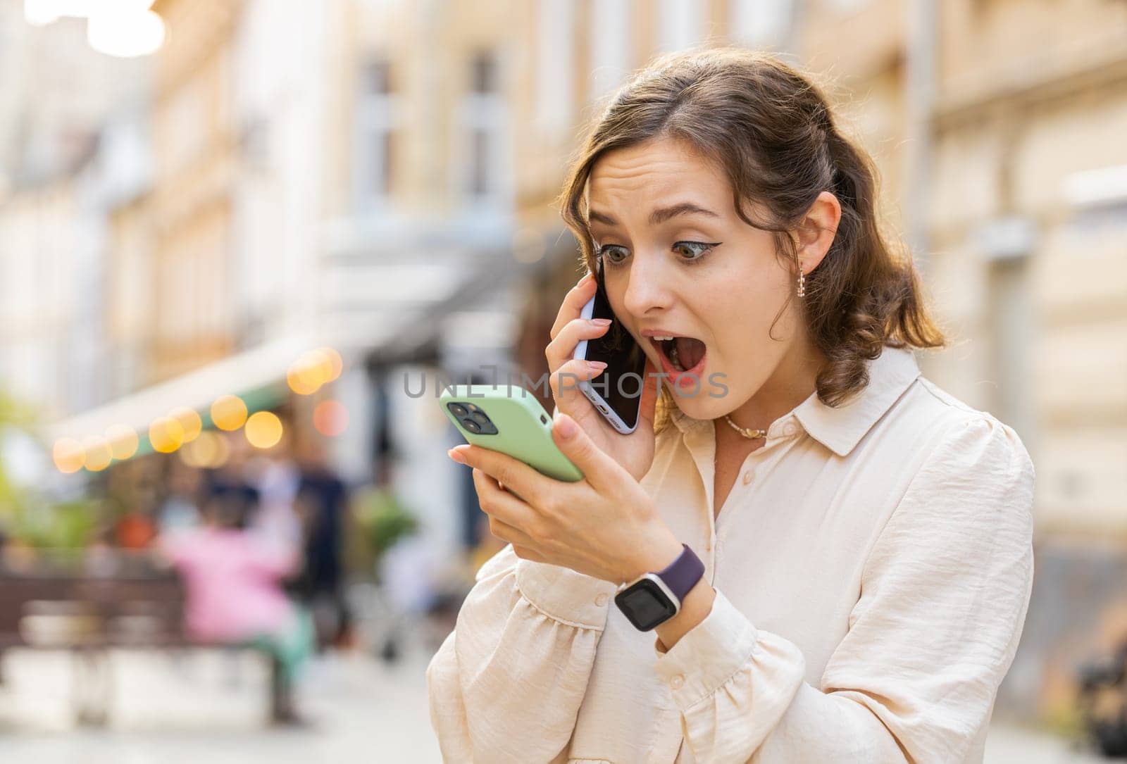 Irritated nervous stressed young woman talking screaming on two mobile phones having conversation conflict quarrel complaint dispute discuss solve problem outdoors. Girl walking in urban city street