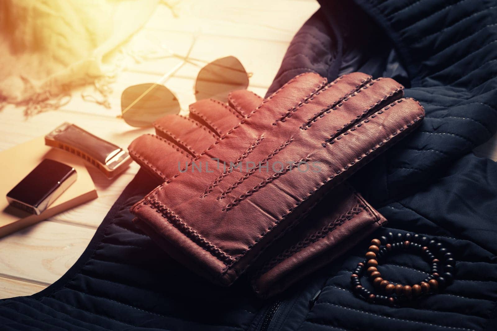 Pair of men's brown leather gloves and other men's accessories on wood background.
