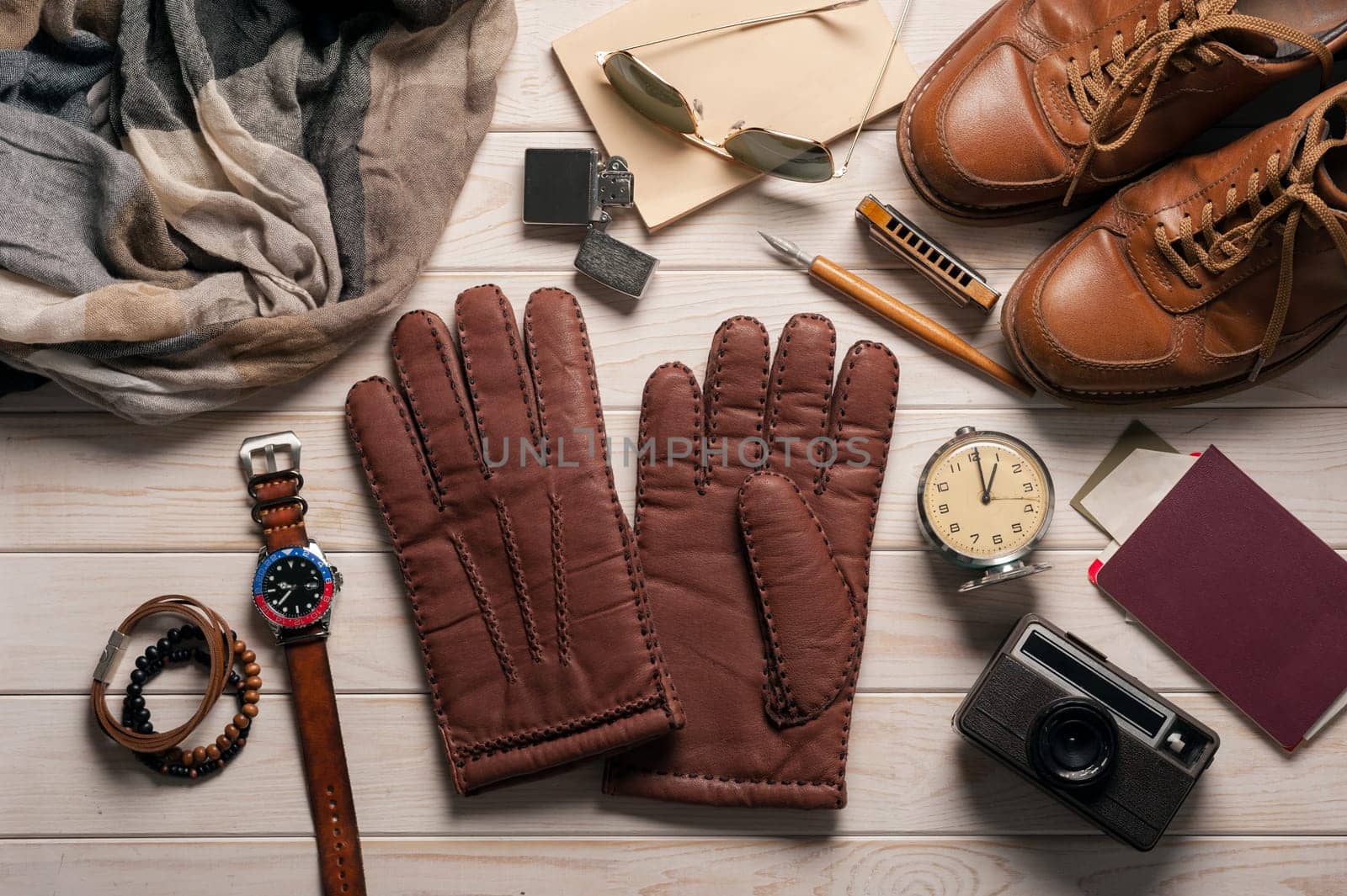 Pair of men's brown leather gloves and other men's accessories on wood background.