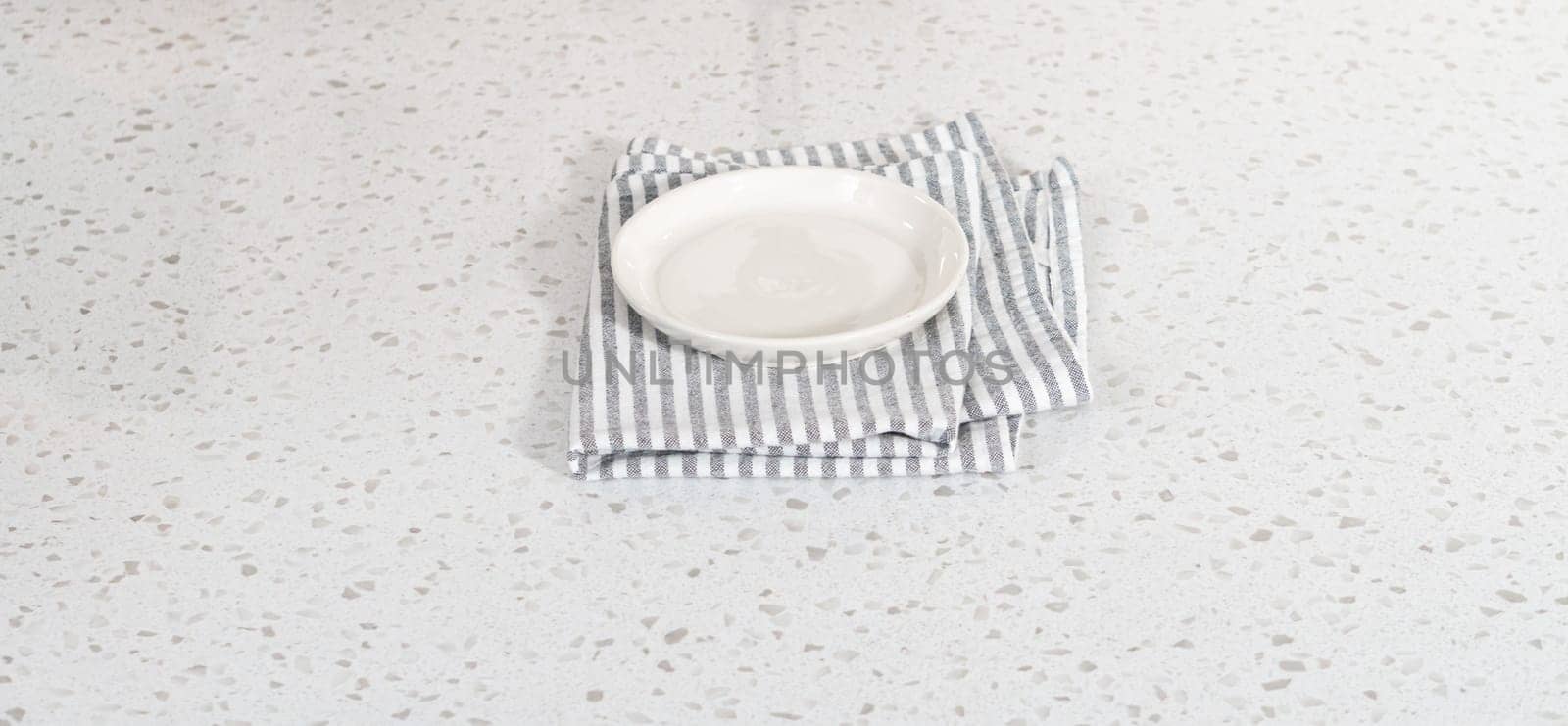 Empty a white plate with a kitchen towel on the white kitchen counter.