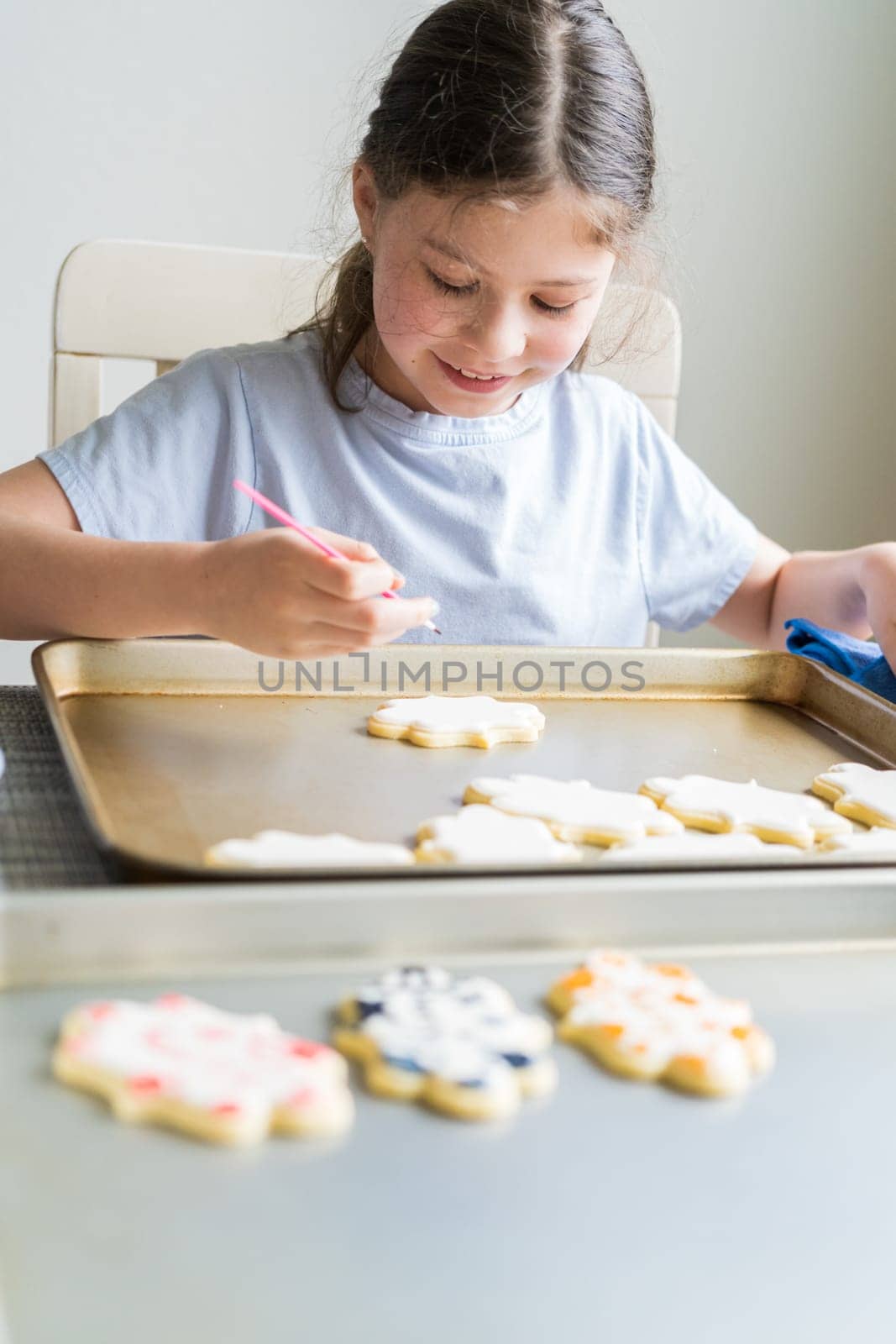 A heartwarming scene of a little girl carefully writing 'Sorry' on sugar cookies with food coloring, the cookies beautifully flooded with white royal icing.