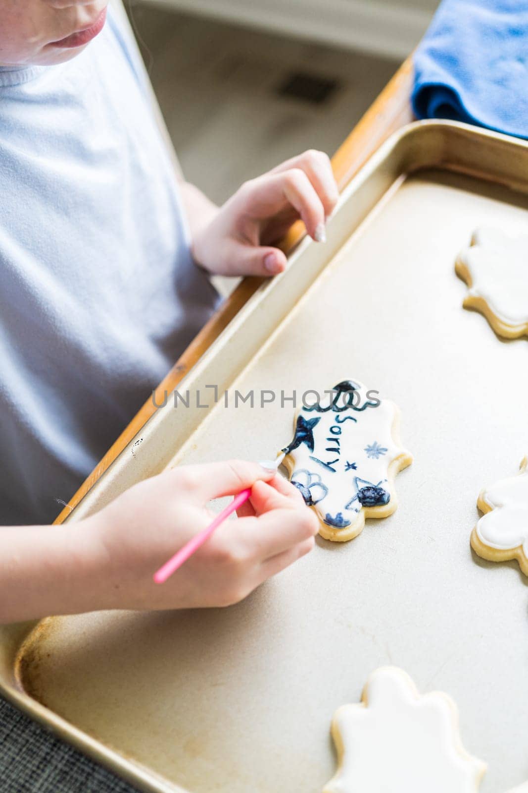 A heartwarming scene of a little girl carefully writing 'Sorry' on sugar cookies with food coloring, the cookies beautifully flooded with white royal icing.