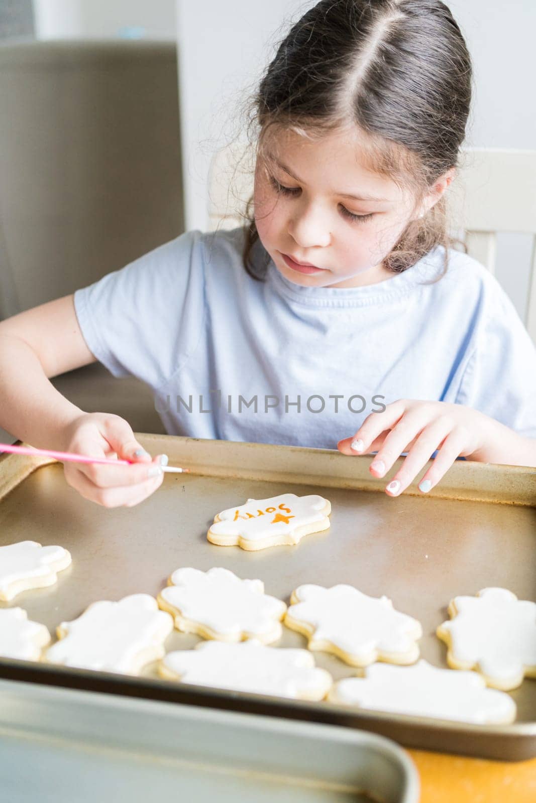 A heartwarming scene of a little girl carefully writing 'Sorry' on sugar cookies with food coloring, the cookies beautifully flooded with white royal icing.