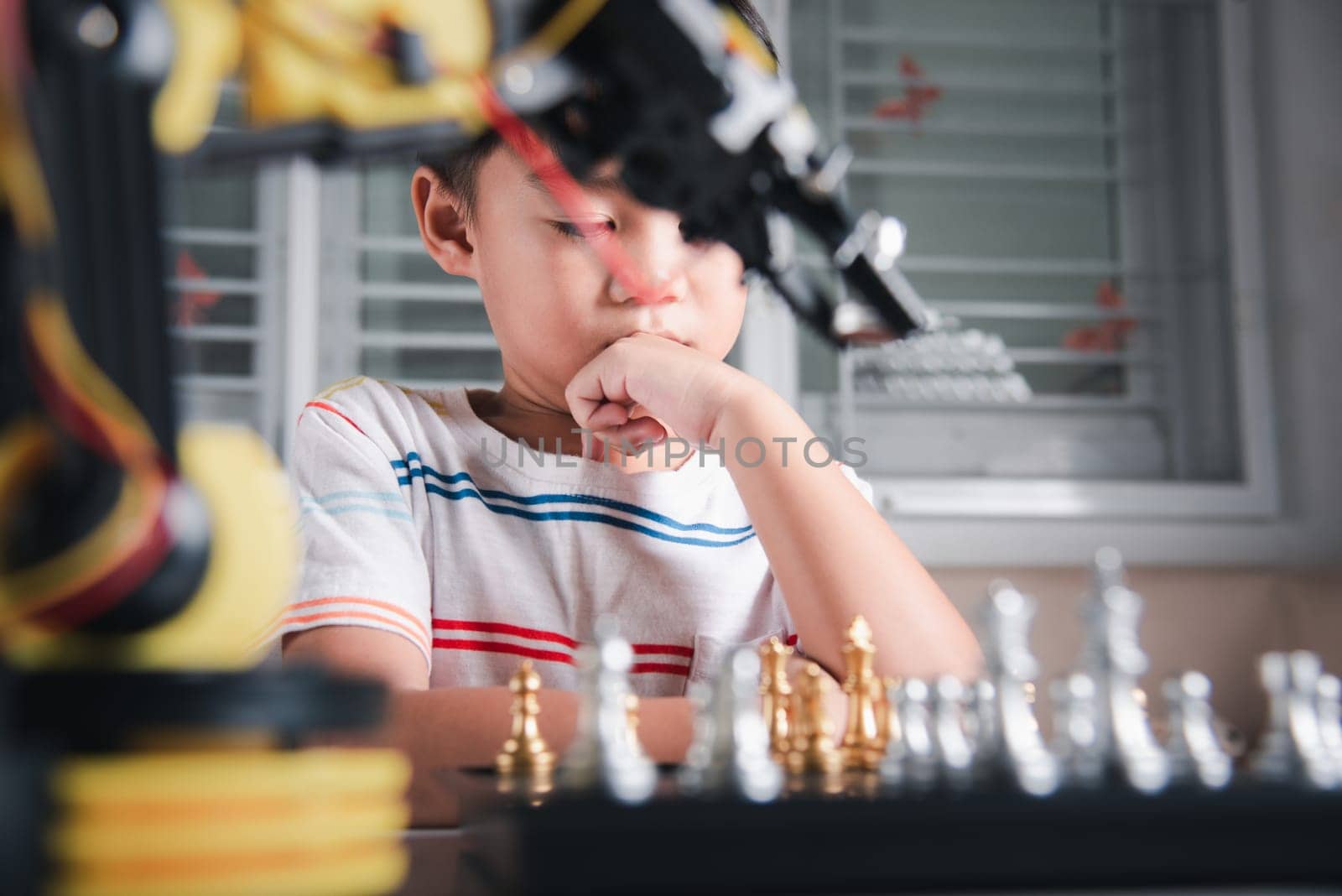 Asian little boy thinking and wait robot arm playing chess by Sorapop